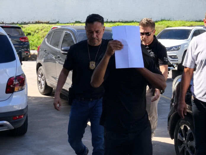 Agente de segurança investigado por exploração sexual de adolescentes chega escoltado por policiais durante cumprimento de mandado em Manaus.